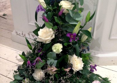 Stående begravningsdekoration med vita och lila blommor.